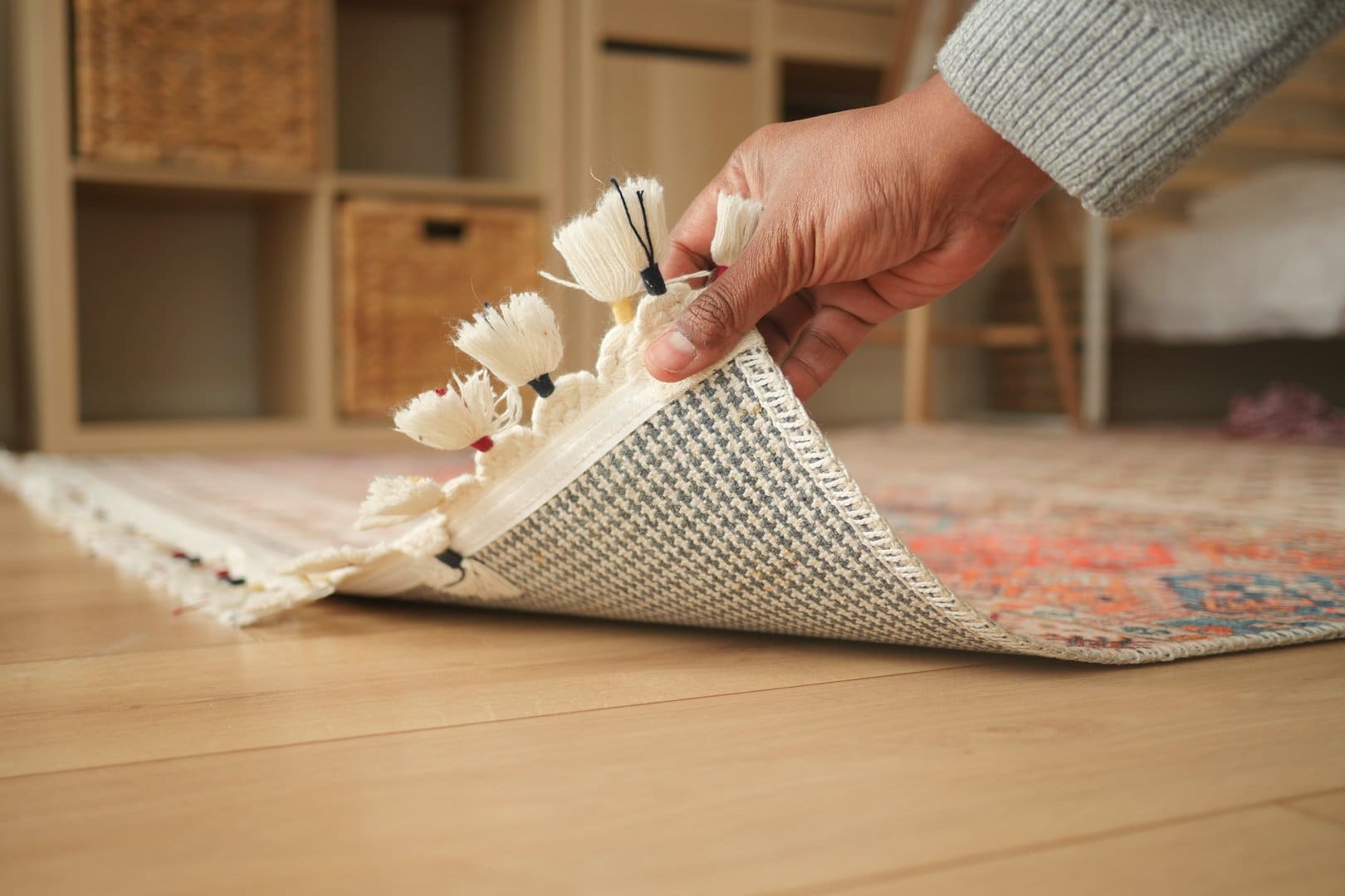 A person is carefully rolling a patterned rug in a bright room