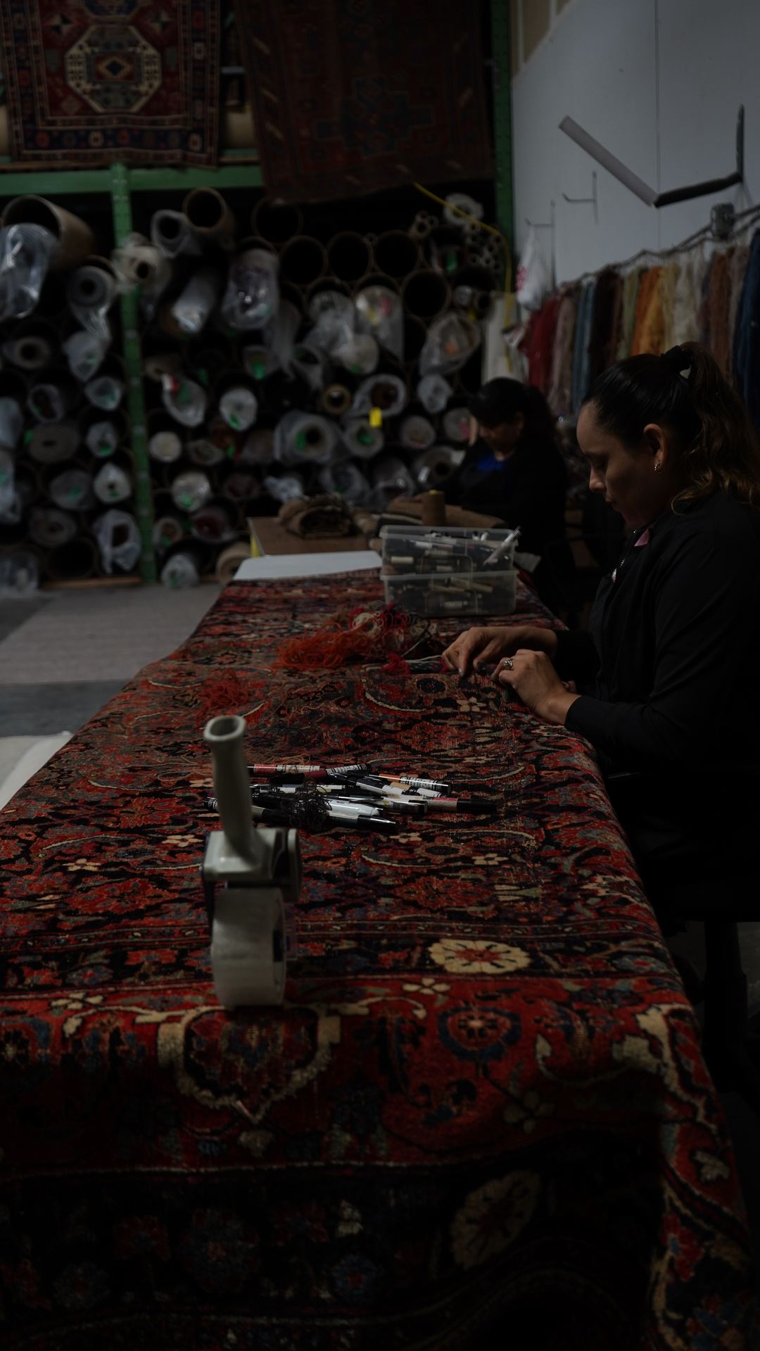 Rug repair artisans hand-stitching the end of a red hand-knotted Oriental rug to secure loose fringe and knots