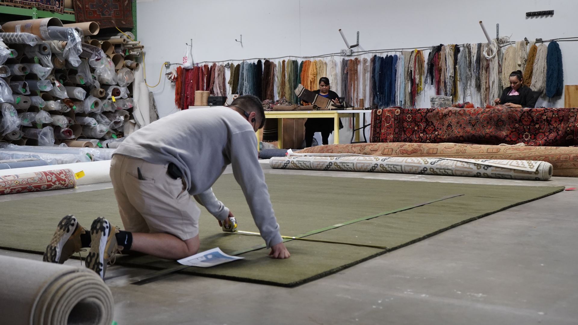 S&S Rug Cleaners technician kneeling to inspect and measure an area rug at the Atlanta cleaning facility before shag rug cleaning begins
