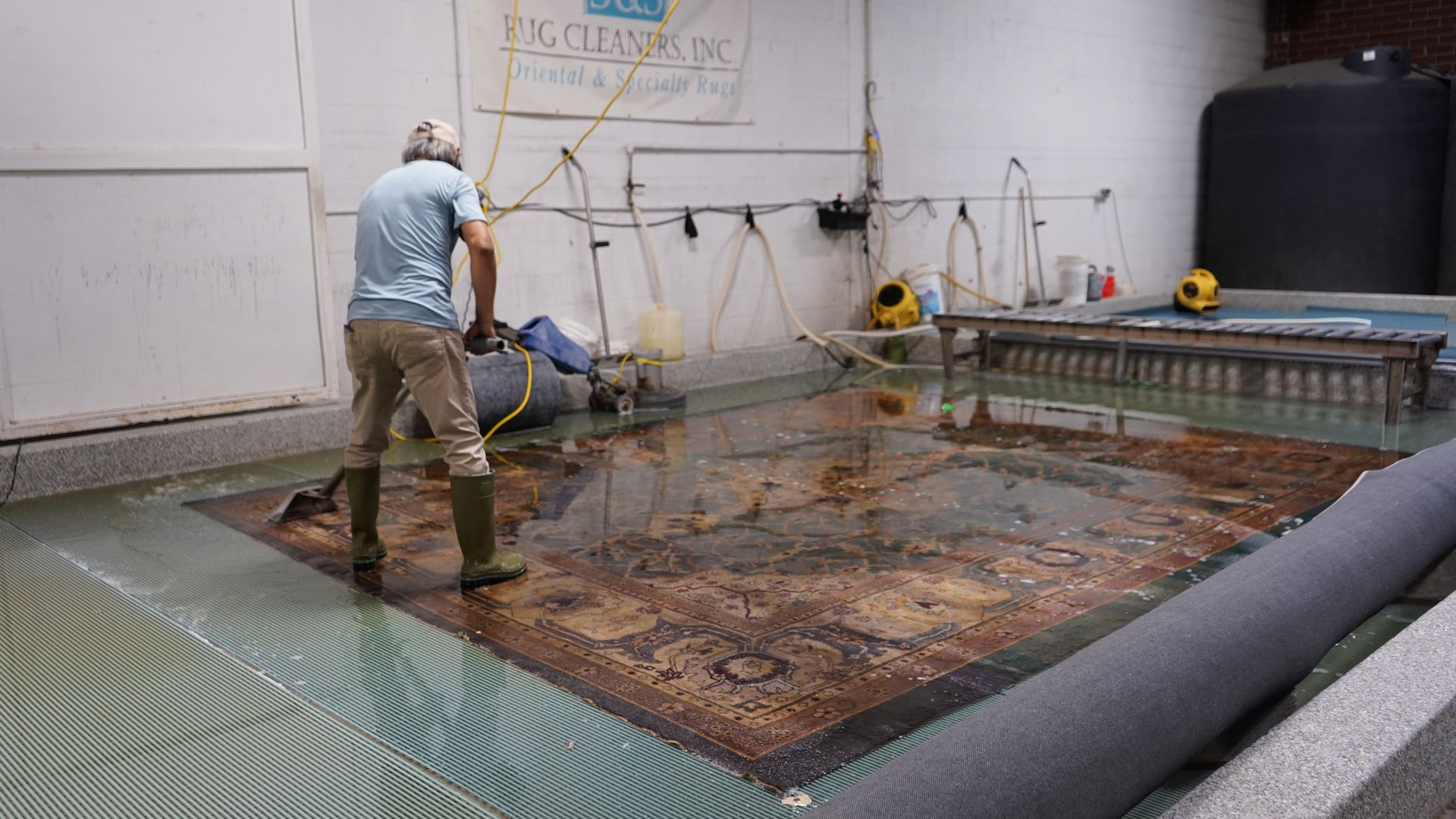 Technician full-immersion washing an area rug in the wash pit at S&S Rug Cleaners in Atlanta to remove mildew and musty odor