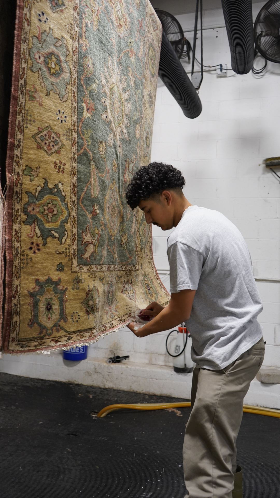 S&S Rug Cleaners technician inspecting the border of a hanging hand-knotted wool rug for color bleeding after washing