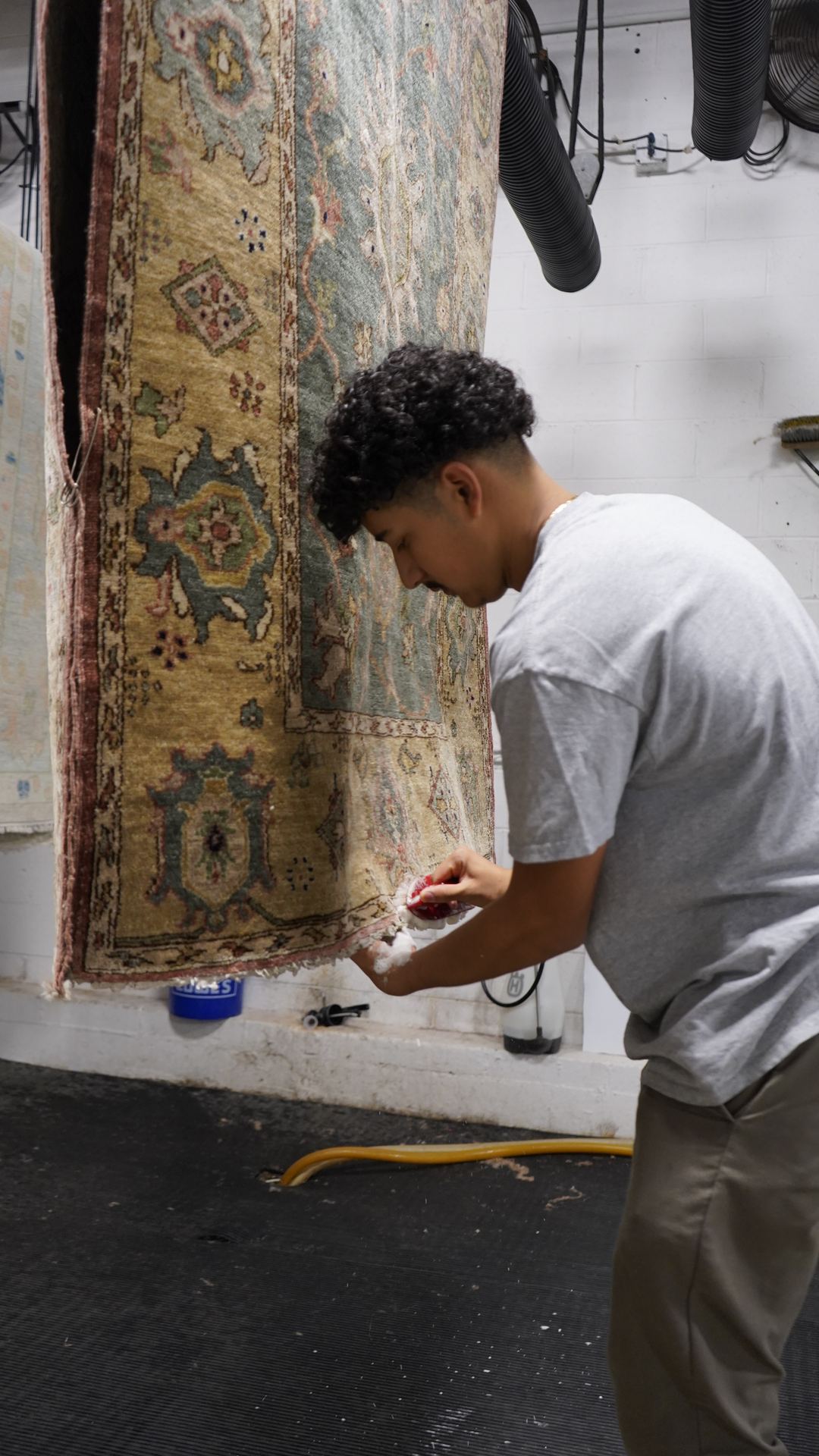 S&S Rug Cleaners technician rinsing and inspecting a hanging wool rug in Atlanta after a deodorizing immersion wash