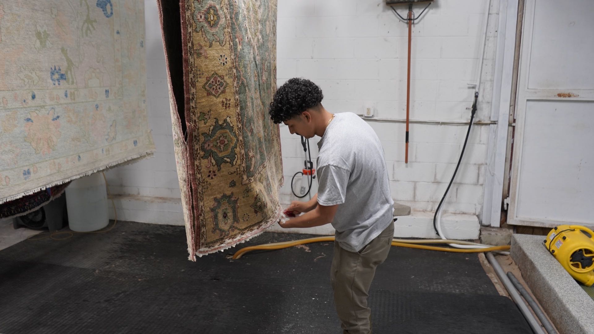 Technician at S&S Rug Cleaners handling a hand-knotted wool rug hung to dry in the Atlanta wash bay after cleaning