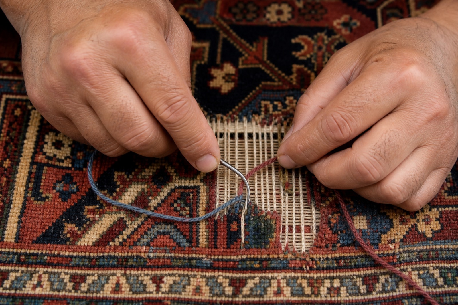 Hand reweaving a damaged area of an antique Oriental rug, tying new knots into the rebuilt foundation with a curved needle