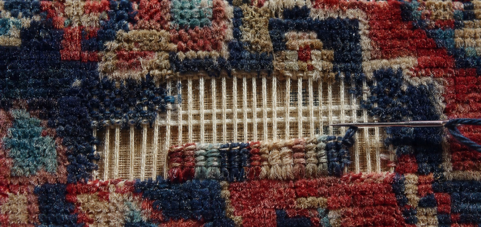 Reweaving in progress on a hand-knotted rug, with new warp and weft threads bridging the hole before fresh knots are tied in
